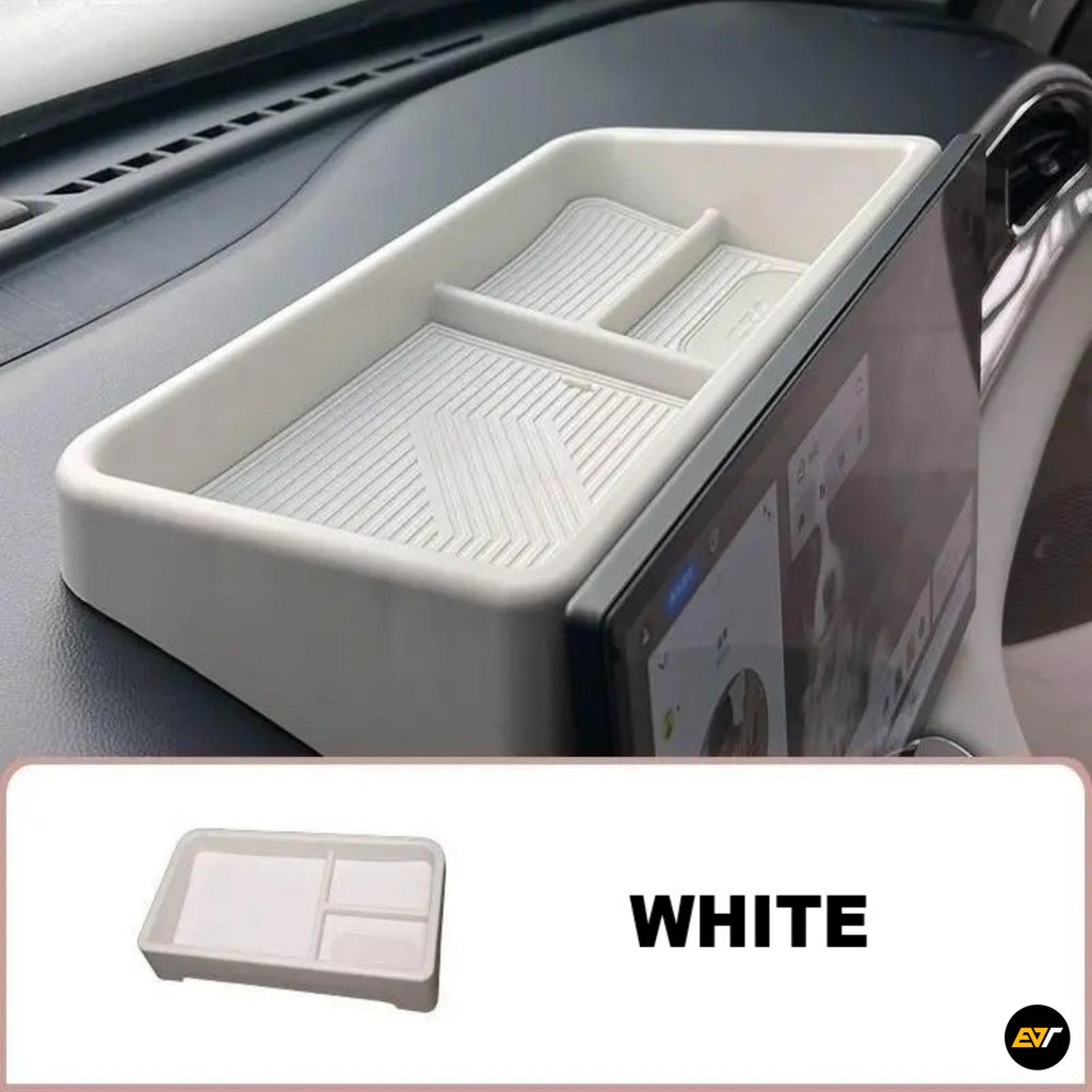 White dashboard storage organiser tray beside an in-car touchscreen, featuring divided compartments and a textured base