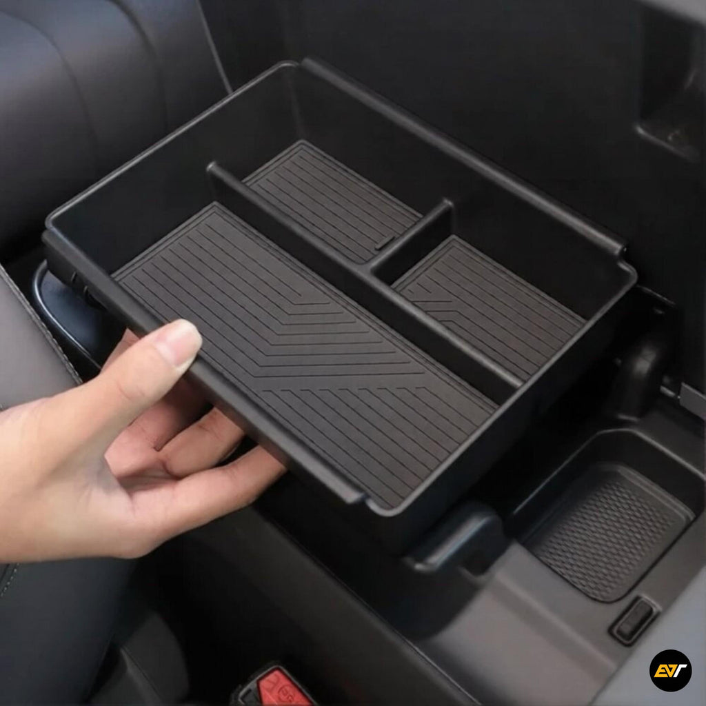 Hand holding a black organiser tray with compartments inside a car centre console storage box for electric vehicles.