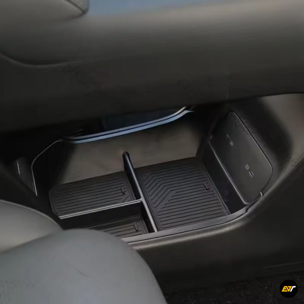 Close-up of a black centre console storage box with divider and rubberised mat in an electric vehicle interior, featuring USB ports on the side panel.