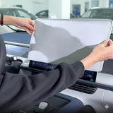 Person fitting a protective grey cover over a large touchscreen navigation display in a car interior