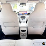 Light-coloured car interior showing rear seats, front seatbacks and centre console with touchscreen infotainment display