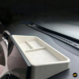 White dashboard storage organiser tray with raised edges and divided compartments fitted inside a vehicle interior