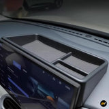 Black car dashboard storage tray with divided compartments and ribbed non-slip liners above a central touchscreen display