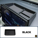 Black car dashboard storage tray with divided compartments and textured non slip inserts beside the central infotainment screen