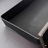 Black centre console storage tray with textured non-slip surface and subtle blue illuminated trim for vehicle interiors