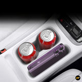 Purple handheld accessory beside two drink cans in a car centre console cup holder area next to the gear selector