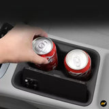 Black car centre console cup holder organiser holding two drinks cans, with a hand placing one inside