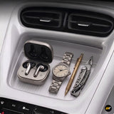 Car centre console storage tray holding wireless earbuds, a metal wristwatch, a brass pen and a folding multi tool