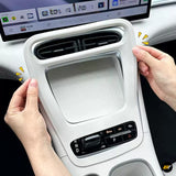 Hands holding a light grey car centre console trim panel with twin air vents, gear selector and climate controls