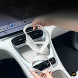 Hands fitting a white protective cover around a car centre console with air vents gear selector and control buttons