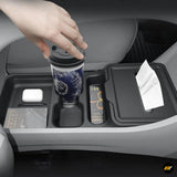 Vehicle centre console storage organiser with cup holder, tissue compartment and accessory slots, shown with a takeaway cup and hand