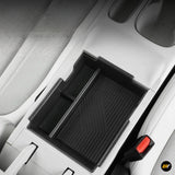 Black rubber centre console storage tray with raised edges and textured liner inside a light coloured car interior