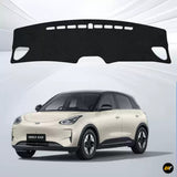 Black dashboard cover shown above a cream Geely EX2 electric car in a studio setting