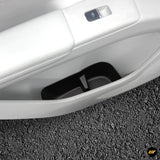 Close-up of a vehicle door storage pocket with black insert, light interior trim and window control button