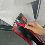 Hand applying a red adhesive strip to black and red vehicle door sill trim beside a white car interior