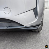 Close-up of a silver car bumper with black lower trim, side detailing and front wheel on an asphalt surface