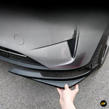 Black front bumper lip spoiler being held against a grey electric vehicle for a sporty exterior upgrade
