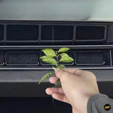 Hand holding a small green plant in front of black car dashboard air vents