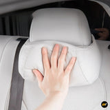 Hand pressing against a white perforated leather car seat with matching headrest inside a vehicle