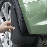 Black car mud flap being positioned beside the rear wheel of a green vehicle for splash protection