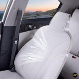White ventilated vehicle seat with airflow arrows beside an open car door and scenic mountain road view