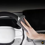 Hand using a grey cleaning cloth to wipe a car steering wheel and dashboard in a modern electric vehicle interior