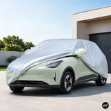 Silver protective car cover draped over a pale green electric vehicle outside a modern home garage