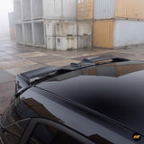 Gloss black aerodynamic roof spoiler fitted to a sleek black vehicle at an industrial shipping container site
