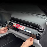 Black glossy car dashboard organiser tray holding small items like a pack of tissues and a lip balm in a modern vehicle interior
