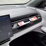 Electric vehicle dashboard storage compartment with glossy black finish holding food packets and a screen display nearby