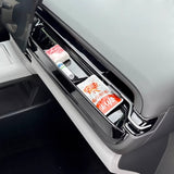 Close-up of a car door storage compartment with a glossy black finish holding personal items and packaging inside.