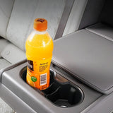 Rear armrest cup holder with a bright orange drink bottle placed inside, featuring black plastic inserts and surrounding grey leather upholstery in a vehicle interior.