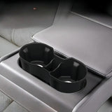 Close-up of a black dual cup holder accessory securely fitted into a grey leather armrest, designed for electric vehicle rear seating.