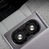 Close-up of rear armrest cup holders integrated into light grey perforated car seats, featuring metallic circular inserts and black trim.
