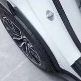 Close-up of black rear mud flap splash guard installed on white electric vehicle near rear wheel and door edge with aerodynamic alloy wheel visible.