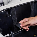 Hand adjusting black protective cover with velcro straps inside a vehicle armrest compartment, close-up detail view