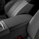 Close-up of a black protective cover on a car armrest between patterned front seats in an electric vehicle interior.