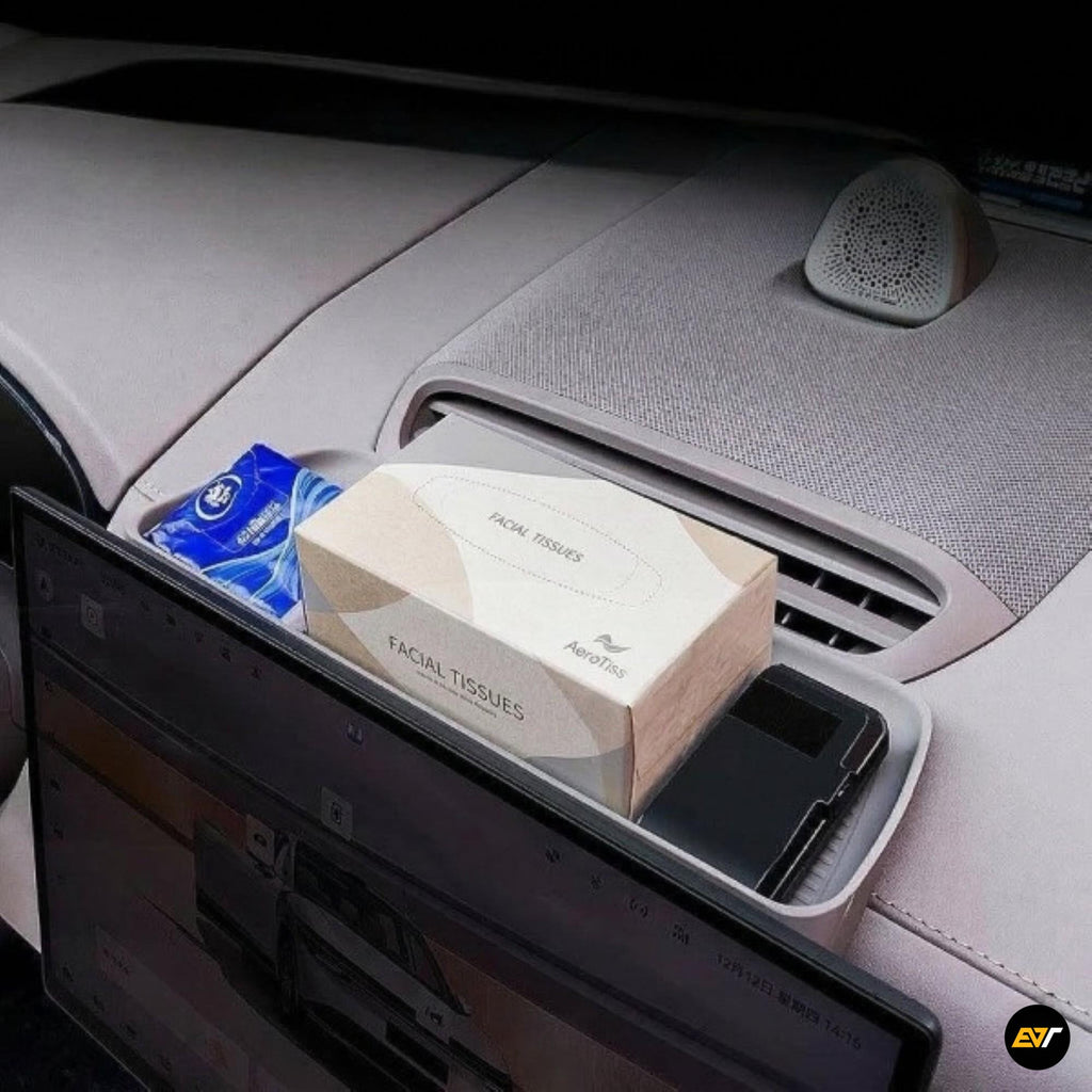 Car dashboard storage box containing facial tissues, wet wipes, and a smartphone behind the navigation screen