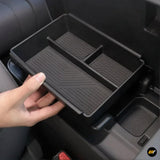 Hand holding a black organiser tray with compartments inside a car centre console storage box for electric vehicles.