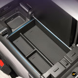 Open centre console armrest storage box with organiser trays inside an electric vehicle interior