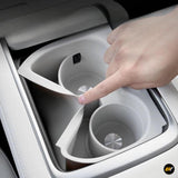 Hand interacting with white plastic cup holder insert in a vehicle centre console, featuring circular grips and metallic details