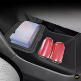 Lower centre console storage compartment in a vehicle holding a pack of wipes and two red soda cans.