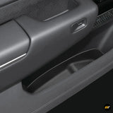 Close-up of vehicle door panel showing black side storage compartment with stitched leather detail and seat adjustment switch