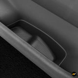 Close-up of a black side storage box inside a vehicle door with textured rubber lining and curved design