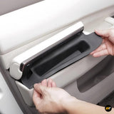 Close-up of hands installing black hidden storage box inside light-coloured electric vehicle door panel accessory