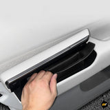 Hand opening hidden storage compartment integrated into white car door panel with black interior trim and chrome handle