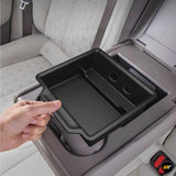 Hand placing black storage tray into rear seat armrest compartment of a light grey electric vehicle interior