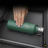 Hand placing green Aqua Vita branded metal water bottle inside black textured vehicle storage organizer tray