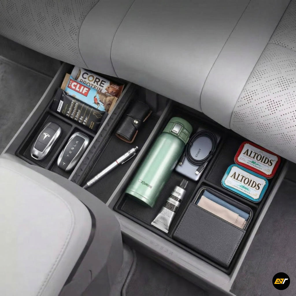 Underseat car organiser tray with compartments holding snacks, keys, water bottle, charger, and wallet inside a grey vehicle interior.