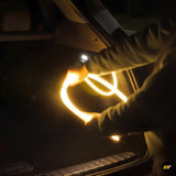Person installing flexible warm white LED light strips inside a vehicle trunk at night for electric car accessory.